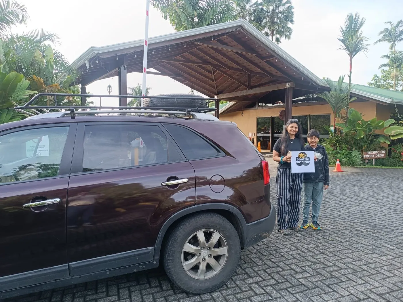 Two travelers holding an Amigo Turista sign next to Gonzalo’s car