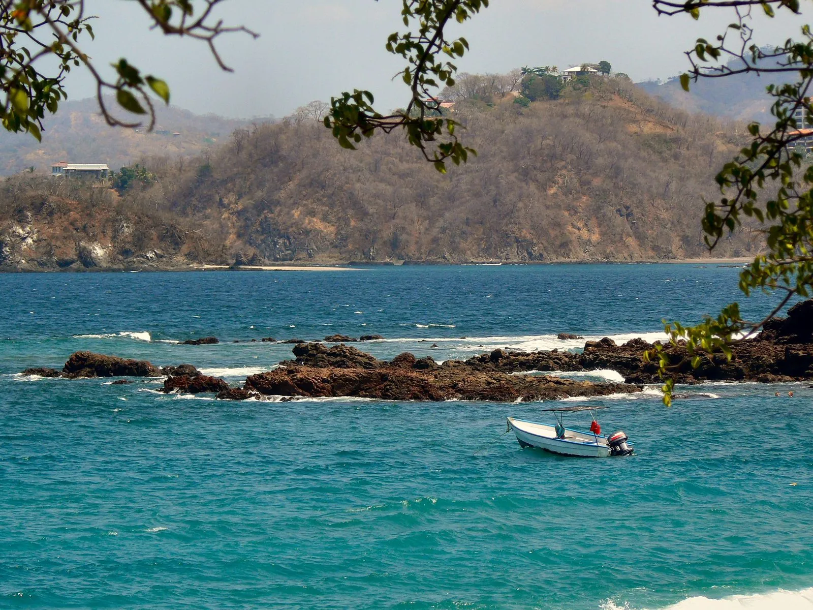 Turquoise water and a rocky point off Playa Conchal, with a small boat at anchor
