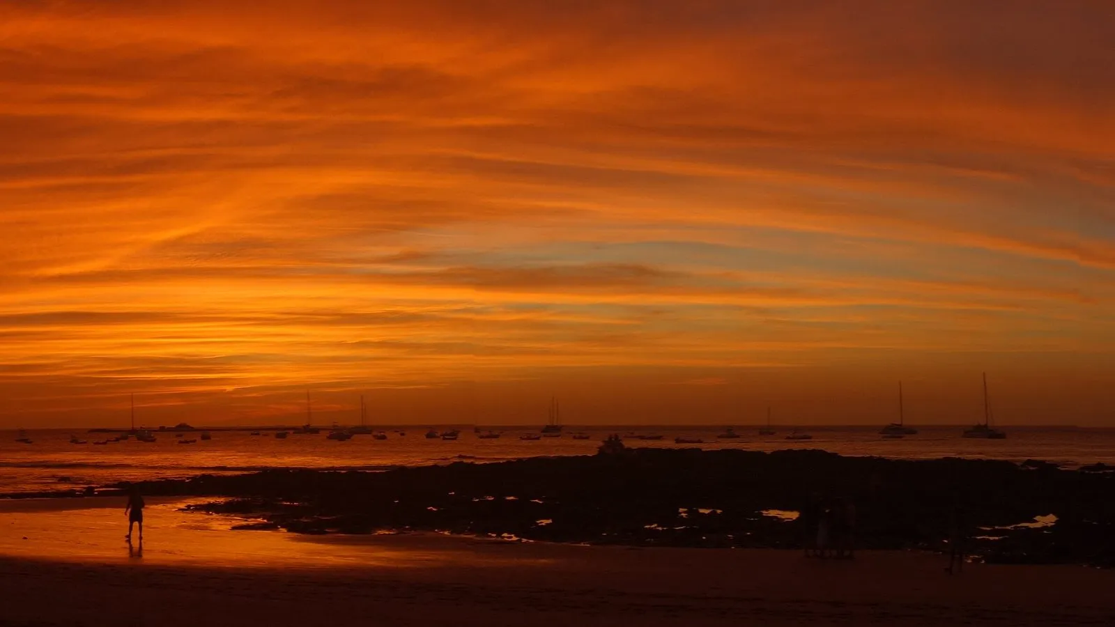 Sailboats anchored in Tamarindo Bay under a fiery sunset (cropped to 16:9 from a wider panorama)
